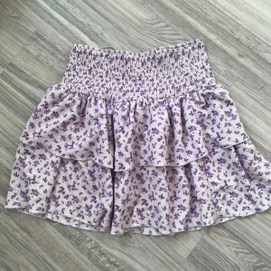 Lila blommig kjol från Gina Tricot - Säljer en superfin lila blommig kjol från Gina Tricot i storlek S. Kjolen har en elastisk midja och volanger. Perfekt för sommaren eller våren! Materialet är mjukt och bekvämt, och mönstret är små blommor i olika nyanser av lila på en ljus bakgrund.💝