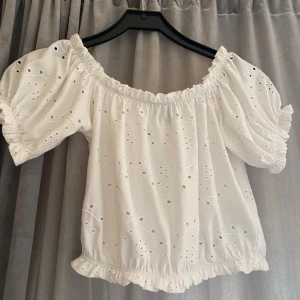 Vit blus med broderade detaljer - Säljer en superfin vit blus med broderade detaljer. Den har en offshoulder-design och korta puffärmar som ger en romantisk känsla. Perfekt för sommardagar eller en mysig vårkväll. Blusen är elastisk vid ärmslut och nederkant för en bekväm passform.