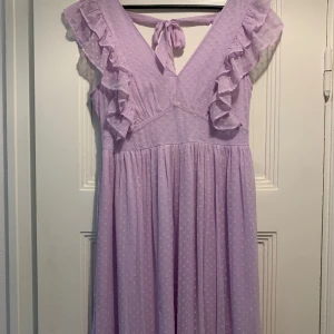 Maxiklänning - En vacker lila maxiklänning med volanger på axlarna och en rosett i ryggen. Klänningen är i en mjukt fallande tyg och har en fin passform. Storlek 40, från Vila. Använd en gång så i mycket gott skick.