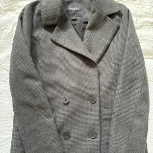 Grå kappa från Monki - Säljer en snygg grå kappa från Monki i storlek XS. Den har ett klassiskt rutigt mönster och är dubbelknäppt med stora knappar. Perfekt för höst och vinter med sin stilrena design och bekväma passform. Kappan är långärmad och i mycket bra skick!