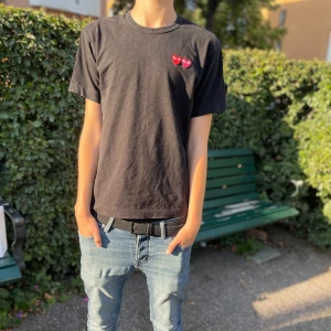 Svart t-shirt från Comme des Garçons - Säljer en svart t-shirt från Comme des Garçons med två röda hjärtan på bröstet. T-shirten är i bomull och har en liten passform M sitter som S passform. Perfekt för en casual look eller att styla upp med en snygg jacka. Använd men i bra skick pris kan diskuteras skriv vid minsta lilla (Kvito finns)