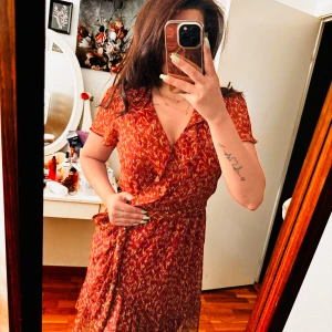 Röd blommig klänning från Lauren Conrad - Säljer en superfin röd blommig klänning från Lauren Conrad. Den är i storlek S och har en omlott-design med ett knytband i midjan. Klänningen har korta ärmar och volangdetaljer vid fållen. Perfekt för sommarens alla fester! 🌸