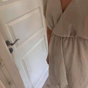 Beige omlottklänning - Säljer en superfin beige omlottklänning med korta ärmar. Perfekt för sommardagar eller en avslappnad fest. Klänningen har en bekväm passform och ett elastiskt band i midjan för en smickrande siluett.