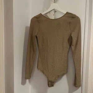 Intimissimi guld body  - En glittrande body med långa ärmar och djup urringning i ryggen från Intimissimi i storlek S, passar S-M. Är i nyskick.