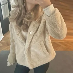 Beige teddyjacka - Mysig och fluffig beige teddyjacka perfekt för kyliga dagar. Jackan har en avslappnad passform med långa ärmar och knappar framtill. Den är supermjuk och har två fickor. OBS!! Jag säljer den på andra bilden! Samma färg ser bara ej ut så på bild ❤️ 