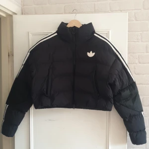 Adidas Originals - Svart vadderad med kort design och tre ränder.  - Inköpt 2022 för 1223 kr från Asos. Använd endast en gång.