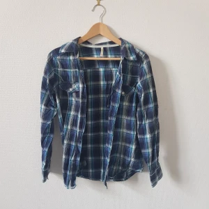 Rutig skjorta från Denim Co. - Rutig skjorta från Denim Co. i storlek L. Skjortan har ett klassiskt rutmönster i blått, grönt och vitt. Den är långärmad och har knappar framtill samt på ärmsluten. 