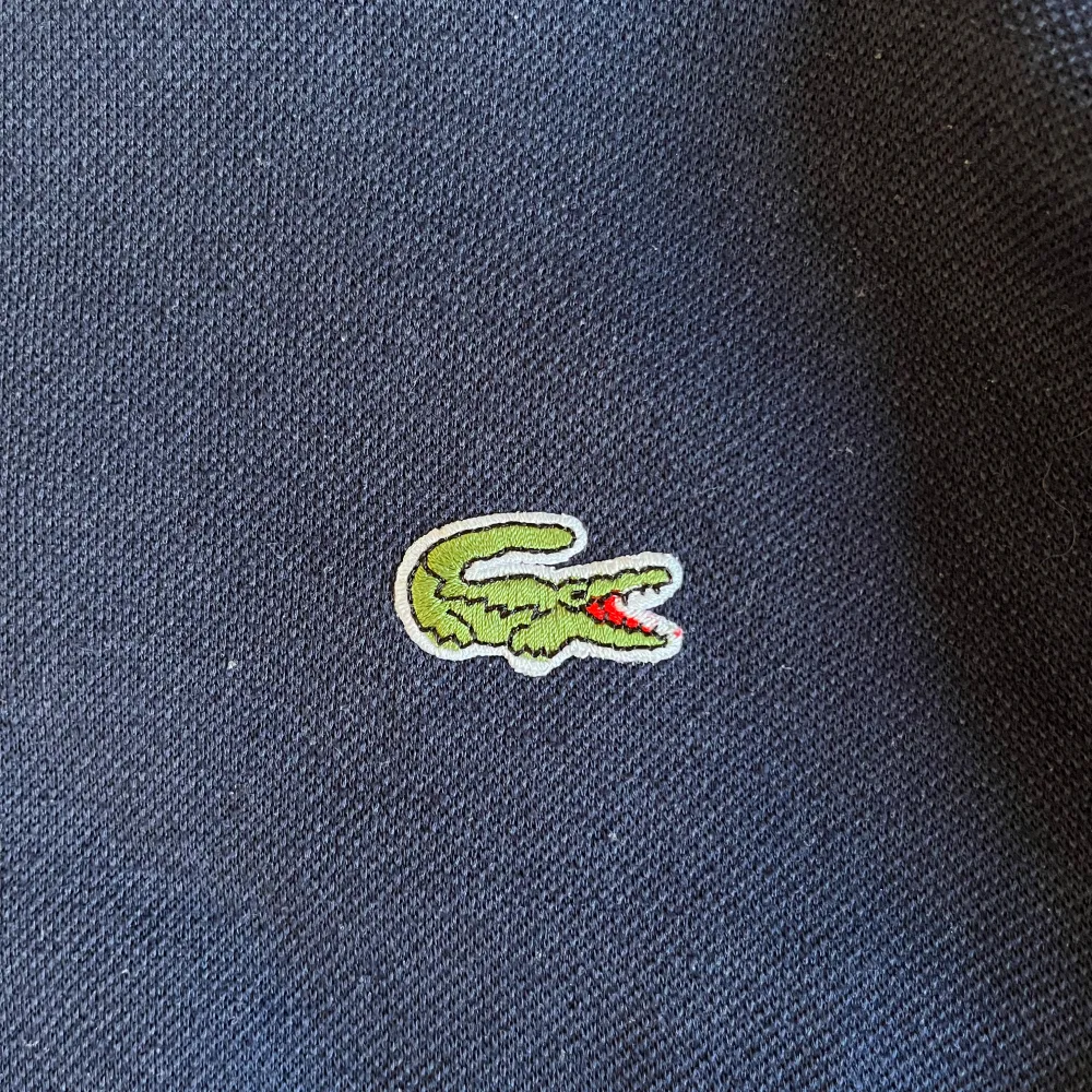 Mörkblå stickad tröja med Lacoste-märke. Saknar dock lappar så kan vara fejk. Har en lös passform och är lite tunnare. Sitter som en XS/S och är lite kortare i modellen. Passar mig som är 1.63m, funkar för längre om man vill ha en mer ”croppad” fit.. Stickat.