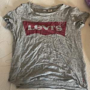 Säljer en grå t-shirt från Levi's i storlek XS. Den har en stor röd logga på framsidan och är gjord i mjukt bomullsmaterial. Perfekt för en avslappnad stil!