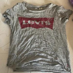 Grå t-shirt från Levi's - Säljer en grå t-shirt från Levi's i storlek XS. Den har en stor röd logga på framsidan och är gjord i mjukt bomullsmaterial. Perfekt för en avslappnad stil!