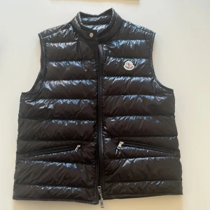 Moncler Gui väst, svart, size 3 - Helt oanvänd moncler gui väst som jag köpte på NK men inte använt då den inte passade mig. Den är i storlek 3/L och man får med prislappar, extra knappar och en moncler påse som ni ser på sista bilden. Nypris: ≈9000kr