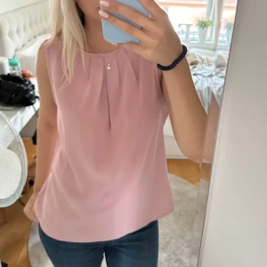 Rosa ärmlös topp - Säljer en söt rosa ärmlös topp i ett tunt och bekvämt material. Toppen har en enkel och stilren design med veckdetaljer vid halsringningen.