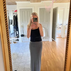 Superskön grå långkjol - En superfin långkjol från Ellos. Den är i ett väldigt skönt och mjukt material som formar på ett snyggt sätt. Det går att välja om man vill ha kjolen låg- eller högmidjat. Oavsett går den till fötterna på mig som är 165cm! 