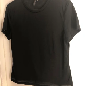 Svart t-shirt från H&M - En klassisk svart t-shirt från H&M i bomull. Perfekt basplagg med rund hals och korta ärmar. Enkel och stilren design som passar till det mesta.Den är lite genomskinlig 