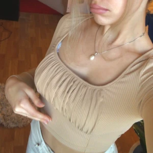 Beige ribbad topp från Shein - Säljer en beige ribbad topp från Shein med långa ärmar och en snygg rynkad detalj framtill. Perfekt för en stilren look. Toppen är i en croppad modell och passar bra till både jeans och kjol.