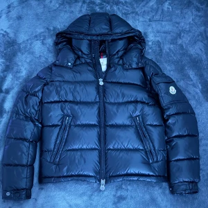 Moncler Maya Jacka - Moncler Maya-jackan är den perfekta blandningen av stil och funktion. Med sitt ikoniska, tidlösa design och exklusiva material håller den dig varm och trendig året runt. En lyxig investering för både kalla vinterdagar och modebevisade outfits. Passar folk runt 170cm+-