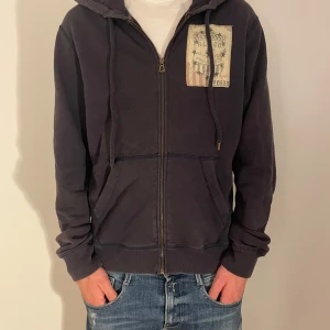 Svart hoodie Ralph Lauren Hoodie - LÄS BESKRIVNINGEN!!!  Säljer en mörkblå hoodie med dragkedja och tryck på både fram- och baksidan. Tröjan har en luva med snörning och långa ärmar. Perfekt för en avslappnad stil. Storlek m och passar en person som är mellan 183/190. Modellen på bilden är 184cm och väger 70 kg.