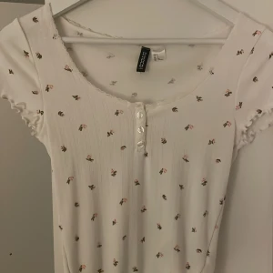  blommig topp  - Söt vit topp från h&m med små blommor och knappar framtill. Den har korta ärmar med volangdetaljer och en rund halsringning. Perfekt för en somrig look!