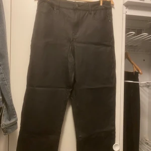 Svarta byxor i fusk skinn - Snygga svarta byxor med klassisk design. De har en rak passform och är perfekta för en stilren look. Byxorna har en dragkedja och knapp framtill.