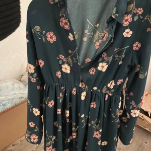 Blommig klänning från Vero Moda - Säljer en vacker blommig klänning från Vero Moda i mörkblått med rosa och beige blommor. Klänningen har långa ärmar och en bekväm passform med markerad midja. Perfekt för både vardag och speciella tillfällen.