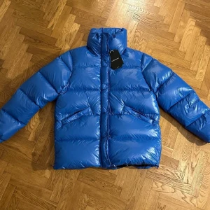 Helt ny!! Peak performance Clara - Helt ny!!  Märke: Peak Performance  Modell: Clara Färg: Blå  Yttertyg: 100% Polyamid Fyllning: 80% Dun och 20% fjäder   Dragkedja och tryckknapp fram Två hand fickor med tryckknapp Hög krage Dragkedja i sidan för att göra den lite extra rymlig 