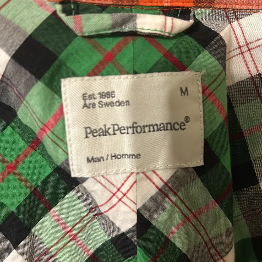 Säljer en färgglad rutig skjorta från Peak Performance i storlek M. Skjortan har ett mönster i orange, blått och svart med knappar framtill och två bröstfickor. Perfekt för en avslappnad stil.. Paidat.