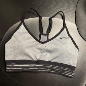 Grå sporttopp från Nike - Snygg grå sporttopp från Nike med svarta detaljer och justerbara axelband. 