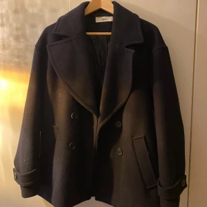Marinblå kappa från ellos - Elegant marinblå kappa från ellos med breda slag och dubbelknäppning. Jackan har långa ärmar och fickor framtill, perfekt för kyligare dagar. En tidlös design som passar till många tillfällen.
