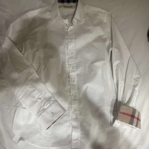Butberry skjorta  - Snygg vit skjorta med klassiska rutiga detaljer på insidan av manschetterna. Skjortan har långa ärmar och knappar framtill. Perfekt för en stilren look. Storlek M men den är liten i storleken så den kan passa S.