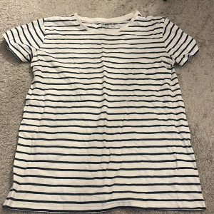 Vit och blå randig t-shirt från Basic You - Säljer en vit och blå randig t-shirt från Basic You i ekologisk bomull. Den har en klassisk rund hals och korta ärmar, perfekt för en avslappnad stil. Passar bra till både jeans och shorts.