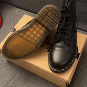 Svarta boots från Dr. Martens - Säljer ett par klassiska svarta Dr. Martens boots med snörning och den ikoniska gula sömmen. Skorna har en robust sula och är perfekta för både stil och komfort. De är nya utan pris lapp!