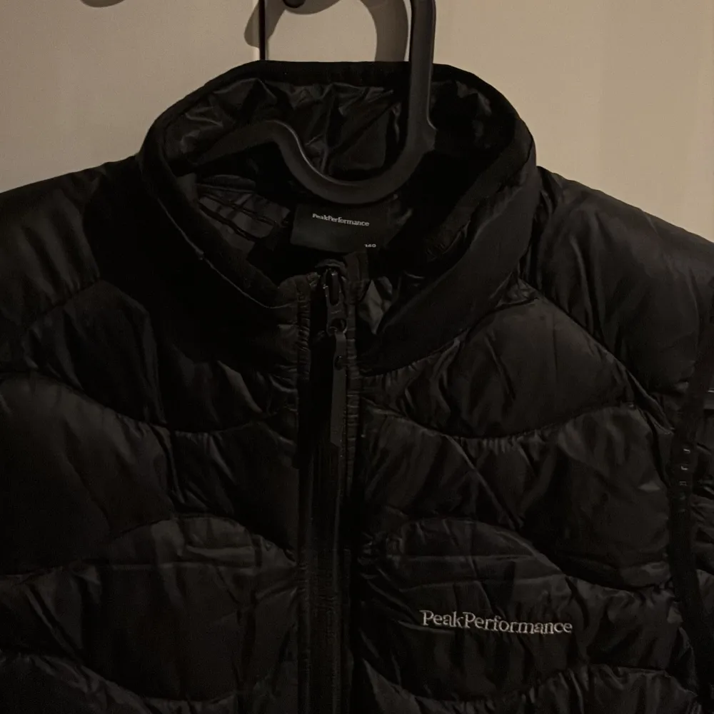 Snygg svart dunväst från Peak Performance med dragkedja framtill. Perfekt för kyligare dagar och ger en sportig look. Västen har en quiltad design och är idealisk för lager-på-lager-stil. Bra skick säljs billigt!!!! Perfekt julklapp!!!. Takit.