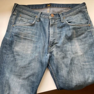 Blå jeans från Lee - Snygga blå jeans från Lee med klassisk femficksdesign och knappgylf. Perfekta för en avslappnad stil. Märkeslogga på bakfickan ger en extra touch.