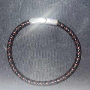 Flätat armband från 7east - Snyggt flätat armband i brunt och svart med ett stilrent magnetlås i silverfärg. Aldrig använt. Perfekt accessoar för en cool och avslappnad stil. 499kr nypris. 