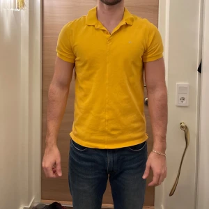 Gul pikétröja från J.Lindeberg - Snygg gul pikétröja från J.Lindeberg i slim fit. Perfekt för en stilren look med korta ärmar och klassisk krage. Liten logga på bröstet ger en extra touch. Passar utmärkt till både jeans och chinos.