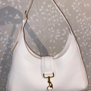 Vit axelväska från H&M - Snygg vit axelväska från H&M Den har en stilren design med guldfärgad spänne och dragkedja. Perfekt för både vardag och fest