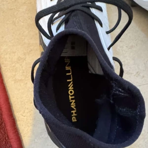 Nike Phantom fotbollsskor - Säljer ett par Nike Phantom fotbollsskor i svart och vitt med gulddetaljer. Skorna har snörning och är i mycket bra skick. Perfekta för fotbollsspelare som vill ha stil och funktion på planen.