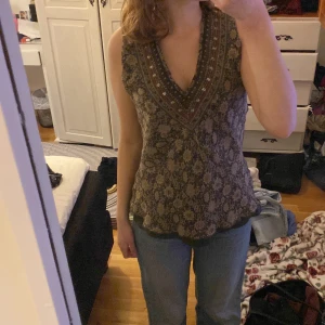 Mönstrad ärmlös topp - Säljer en snygg ärmlös topp med ett detaljerat mönster i jordnära färger. Toppen har en v-ringad design och är perfekt för både vardag och fest. Den är i bra skick och passar perfekt till jeans för en avslappnad look.