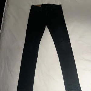 Svarta jeans från Dondup  - Säljer ett par svarta jeans från George i storlek 30. De har en slim passform och är perfekta för både vardag och fest. Jeansen är i bra skick och har en klassisk design med fem fickor och knappgylf. Perfekta för höst och vinter!