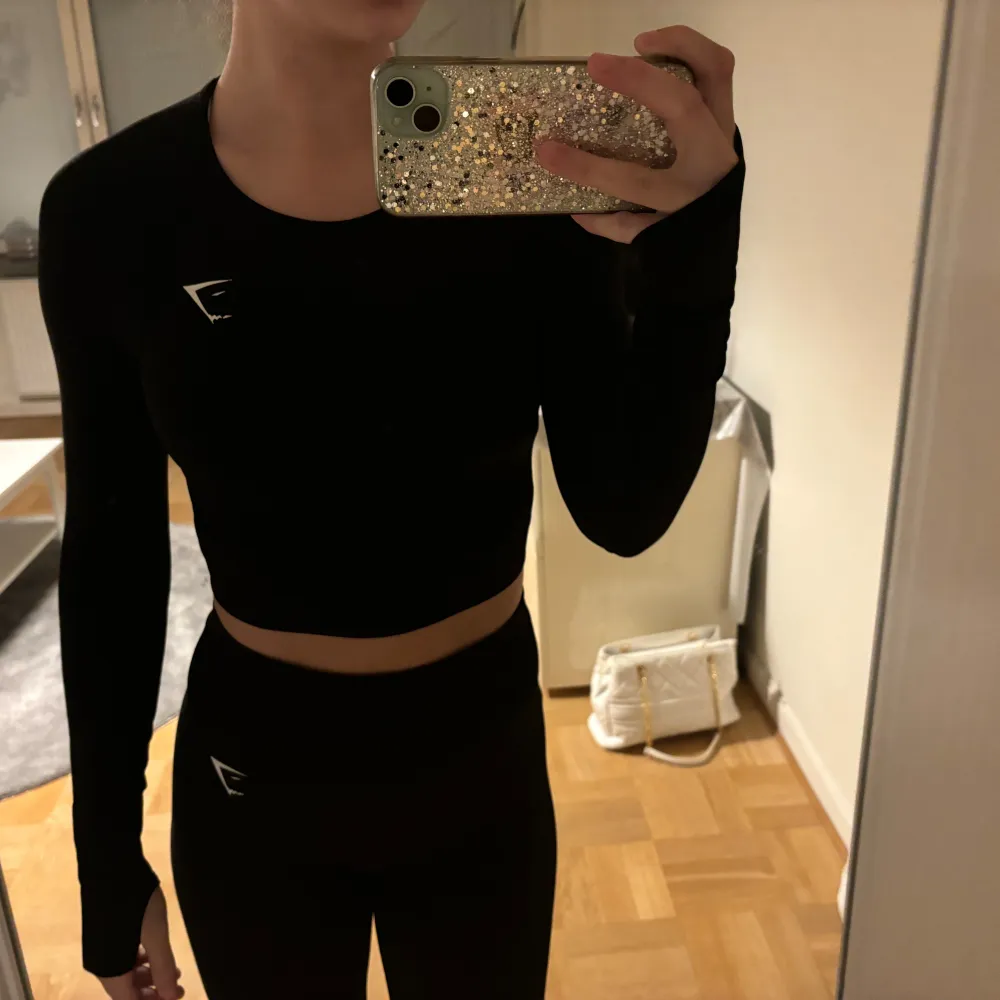 Säljer en svart croppad träningstopp från Gymshark i mycket bra skick. Toppen är tight och har långa ärmar, perfekt för gymmet eller löprundan. Den är gjord i ett stretchigt material som andas bra. Snygg och funktionell för alla träningspass!. Toppar.