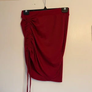Röd kjol med snörning - Snygg röd kjol med cool snörningsdetalj på sidan som ger en unik look. Perfekt för både vardag och fest! Kjolen har en tight passform och är gjord i ett mjukt material som känns skönt mot huden. Ett måste i garderoben för dig som vill sticka ut!