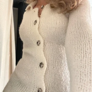 Vit stickad kofta med band - Superfin vit stickad kofta med stora knappar och ett bälte i midjan. Köpte den från zara förra året o finns inte kvar hos dem längre! Man kan ha den både m bältet och utan, man kan även knyta back bältet så de bara sitter därbak! Knappt andvänd!