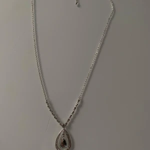 Elegant halsband med droppformad hängsmycke - Säljer ett elegant halsband med en droppformad hängsmycke. Halsbandet är i silverfärg och har en glittrig detalj runt hängsmycket. Perfekt för festliga tillfällen eller som en fin present. 💎