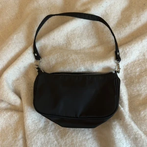 Svart axelväska från Gina Tricot - Snygg och praktisk svart axelväska från Gina Tricot i mycket bra skick. Väskan har en dragkedja upptill och är perfekt för vardagsbruk. Den är stilren och lätt att matcha med olika outfits.