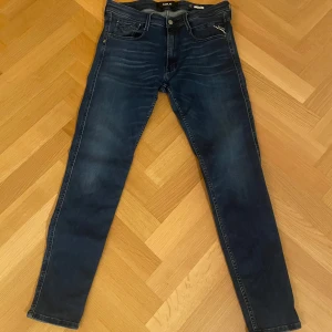 Mörkblå jeans från Replay - Säljer ett par snygga mörkblå jeans från Replay i mycket bra skick. De har en slim passform och är perfekta för både vardag och fest. Jeansen har klassiska fem fickor och en knappgylf. Märkesloggan syns tydligt på bakfickan och etiketten. Perfekta för dig som vill ha en stilren look! Säljer dessa för endast 449 kr då nypriset ligger idag på 1999 kr! 