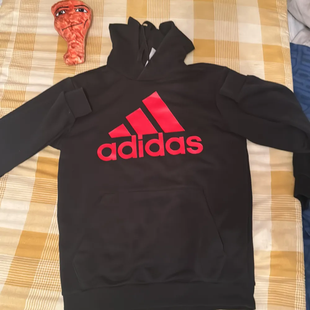 Säljer en svart hoodie från Adidas med röd logga på bröstet. Den är i bra skick och perfekt för höst och vinter. Tröjan har långa ärmar och en klassisk känguruficka framtill. Perfekt för träning eller chill dagar. Med ett par byxor. Tröjan 174 och byxorna 174.. Tröjor & Koftor.