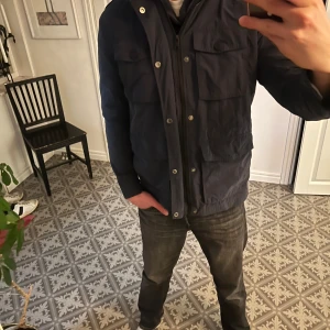 Mörkblå jacka med dragkedja och knappar - Säljer en snygg mörkblå jacka i bra skick. Den har både dragkedja och knappar framtill, vilket ger extra skydd mot kyla. Jackan har flera praktiska fickor och en hög krage. Perfekt för höst och vår! 🧥