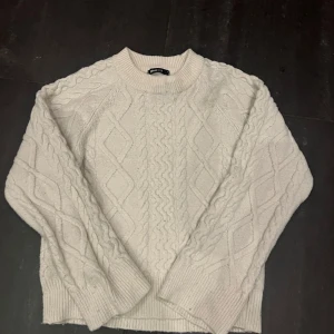 Beige stickad tröja från Gina Tricot - Mysig vit stickad tröja från Gina Tricot. Perfekt för kyliga dagar med sitt snygga flätmönster och ribbade kanter. Den har en klassisk rund hals och långa ärmar. Superfin att matcha med jeans eller kjol för en avslappnad look. Nypris 399kr 