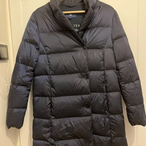 Svart dunjacka från GANT - Säljer en snygg svart dunjacka från GANT i mycket bra skick, men tror att bätle saknas.Jackan är lång och perfekt för höst och vinterdagar. Den har långa ärmar och stängs med knappar framtill. Stilren och varm, perfekt för både vardag och festliga tillfällen. Storlek 36 eller 38.