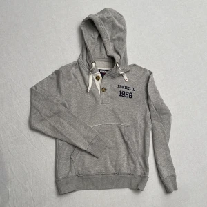Grå hoodie från Bondelid - Säljer en unik snygg grå hoodie från Bondelid i storlek S. Den har en klassisk design med knappar. Perfekt för en avslappnad stil och passar bra till både jeans och joggers. Huvan har snören för justering. Använd ett fåtal gånger, så den är i mycket bra skick. ”Slitningarna” är del av designen